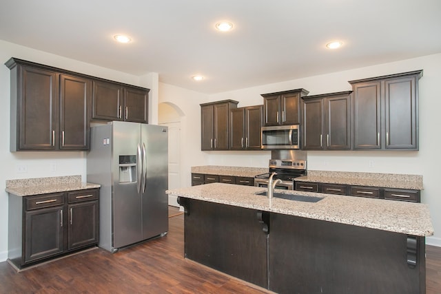 kitchen featuring dark brown cabinetry, stainless steel appliances, sink, dark hardwood / wood-style flooring, and a center island with sink