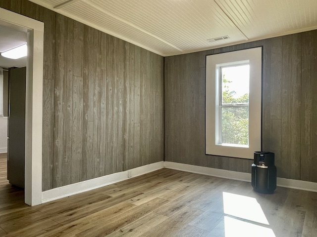 unfurnished room featuring wood walls, hardwood / wood-style floors, and a healthy amount of sunlight