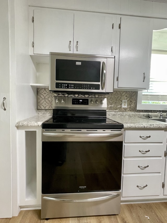 kitchen featuring light wood-type flooring, tasteful backsplash, white cabinetry, appliances with stainless steel finishes, and light stone countertops