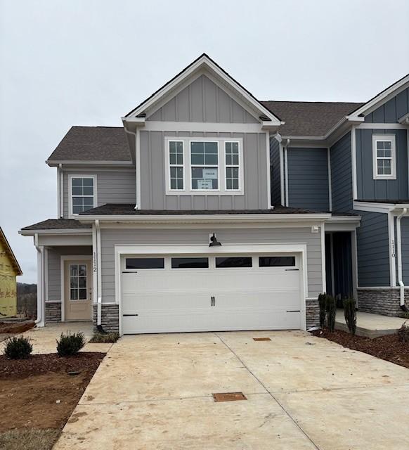 view of front of property with an attached garage, stone siding, driveway, and board and batten siding