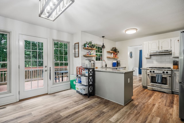 kitchen featuring decorative light fixtures, decorative backsplash, high end stove, light hardwood / wood-style floors, and white cabinetry