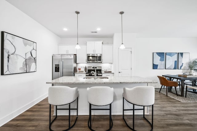 kitchen featuring pendant lighting, stainless steel appliances, white cabinets, light stone countertops, and a kitchen island with sink