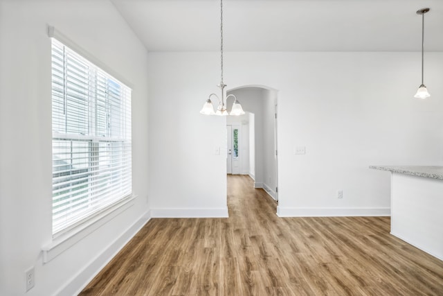 unfurnished dining area featuring wood-type flooring, a notable chandelier, and a healthy amount of sunlight