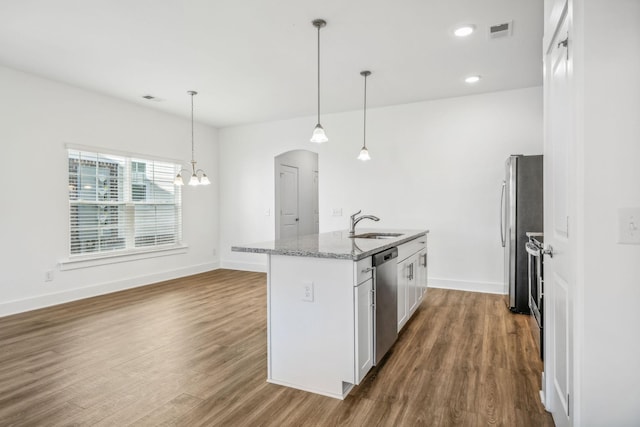 kitchen featuring stainless steel appliances, stone counters, decorative light fixtures, white cabinetry, and a kitchen island with sink