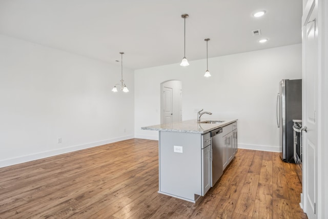 kitchen with light wood-type flooring, hanging light fixtures, a kitchen island with sink, and stainless steel appliances