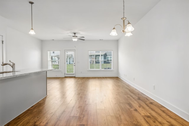 unfurnished living room featuring a wealth of natural light, ceiling fan with notable chandelier, and light wood-type flooring