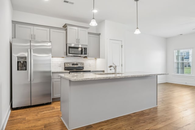 kitchen featuring stainless steel appliances, light hardwood / wood-style flooring, decorative backsplash, an island with sink, and gray cabinets