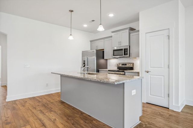 kitchen featuring decorative light fixtures, stainless steel appliances, a kitchen island with sink, and light stone countertops