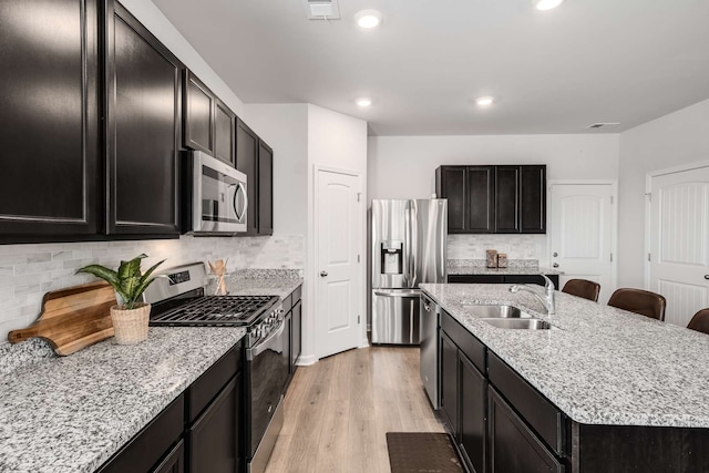 kitchen with sink, light wood-type flooring, a kitchen island with sink, tasteful backsplash, and stainless steel appliances