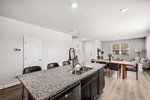 kitchen with sink, light stone counters, a center island with sink, light wood-type flooring, and a breakfast bar area