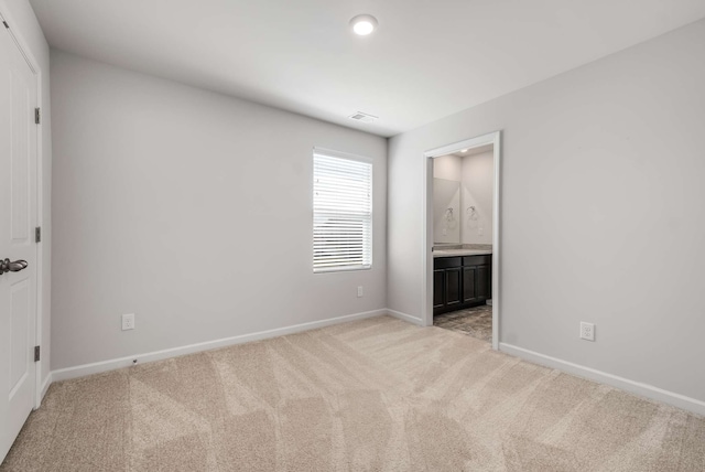 unfurnished bedroom with ensuite bathroom and light carpet