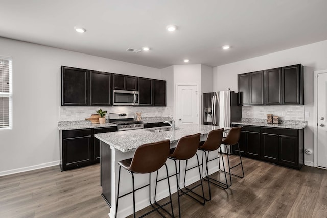 kitchen with tasteful backsplash, a kitchen island with sink, hardwood / wood-style flooring, a breakfast bar area, and stainless steel appliances