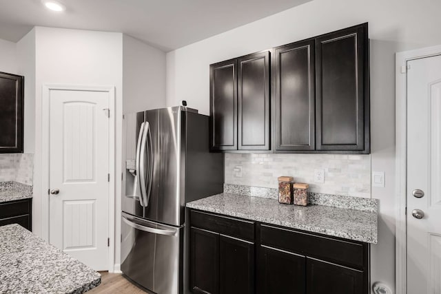 kitchen featuring light stone counters, light hardwood / wood-style floors, decorative backsplash, and stainless steel refrigerator with ice dispenser