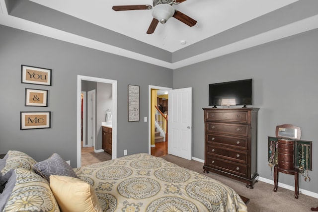 carpeted bedroom with ceiling fan, a raised ceiling, and ensuite bathroom