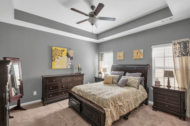 carpeted bedroom with ceiling fan and a raised ceiling