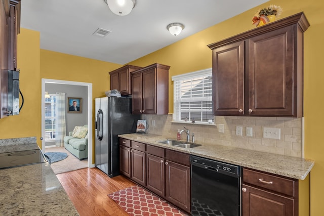 kitchen with backsplash, light hardwood / wood-style floors, sink, light stone counters, and black dishwasher