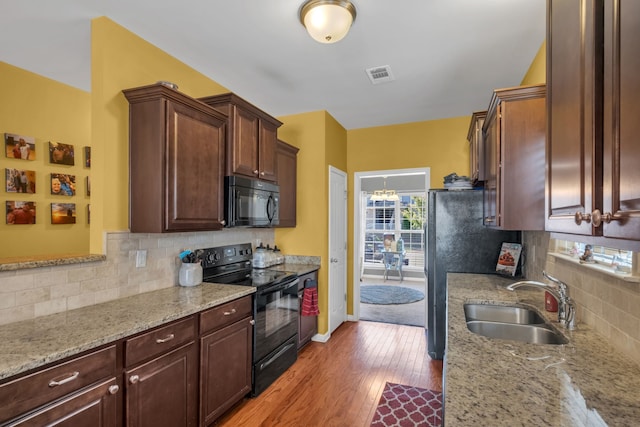 kitchen with tasteful backsplash, sink, light stone counters, black appliances, and light wood-type flooring