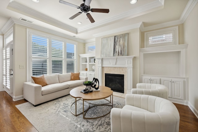 living room with a tray ceiling, a tile fireplace, crown molding, and dark hardwood / wood-style flooring