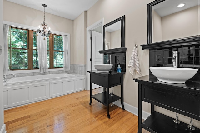 full bathroom featuring two vanities, wood finished floors, a sink, a chandelier, and a bath