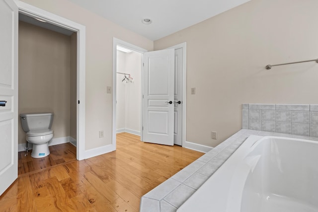 full bath featuring baseboards, toilet, a bath, and wood finished floors