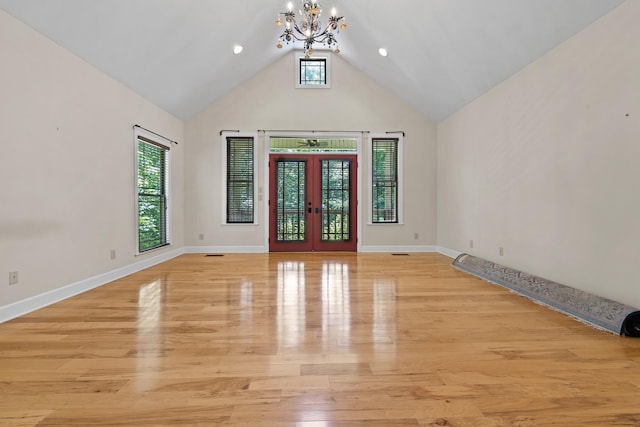 empty room with french doors, light wood-style flooring, an inviting chandelier, high vaulted ceiling, and baseboards