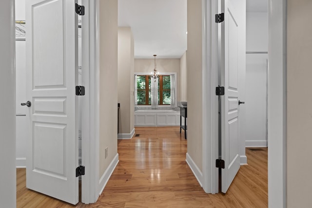 hall with light wood-type flooring, baseboards, and an inviting chandelier