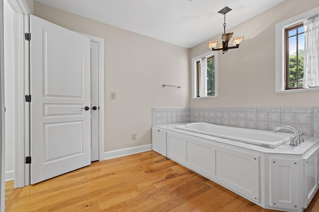 bathroom featuring a healthy amount of sunlight, baseboards, wood finished floors, and a bath