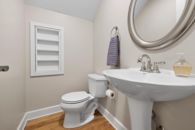 half bath featuring a sink, wood finished floors, toilet, and baseboards