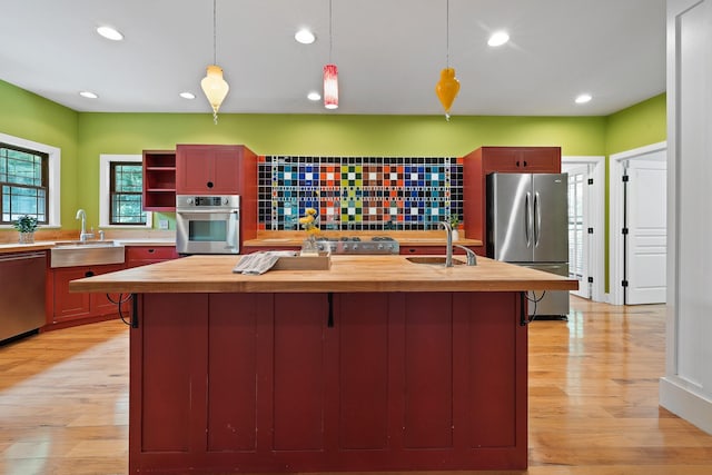 kitchen featuring decorative light fixtures, open shelves, appliances with stainless steel finishes, a kitchen island with sink, and a sink
