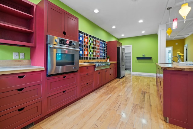 kitchen with hanging light fixtures, stainless steel appliances, light countertops, light wood-style floors, and open shelves