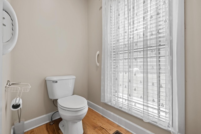half bathroom with wood finished floors, toilet, and baseboards