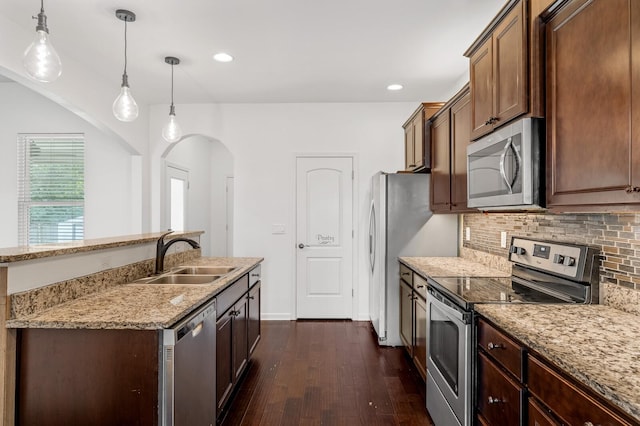 kitchen featuring sink, light stone counters, backsplash, decorative light fixtures, and appliances with stainless steel finishes