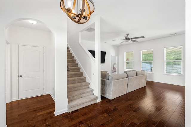 unfurnished living room featuring ceiling fan with notable chandelier and dark wood-type flooring