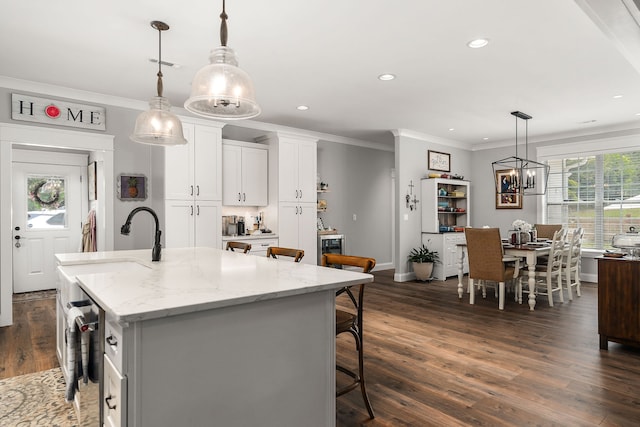 kitchen with a kitchen breakfast bar, dark wood-type flooring, a kitchen island with sink, white cabinetry, and light stone counters