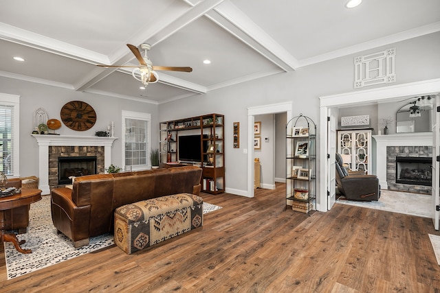 living room with ceiling fan, beam ceiling, wood-type flooring, and a stone fireplace