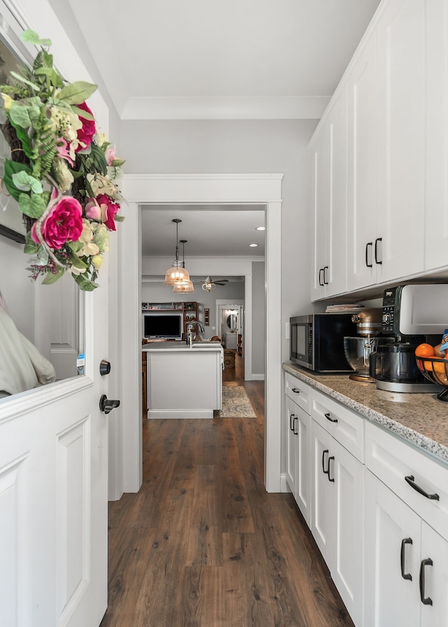 kitchen featuring ornamental molding, dark hardwood / wood-style flooring, light stone counters, ceiling fan, and white cabinets