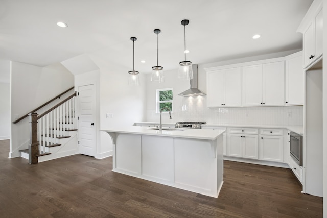 kitchen with sink, dark wood-type flooring, a center island with sink, wall chimney range hood, and white cabinets