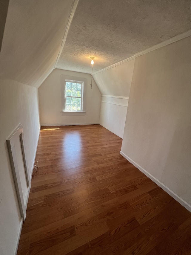 additional living space featuring a textured ceiling, vaulted ceiling, and wood finished floors