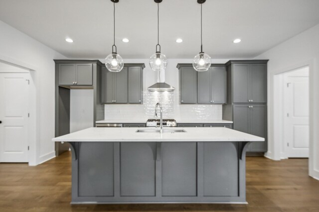 kitchen with decorative backsplash, gray cabinets, a center island with sink, and dark hardwood / wood-style flooring