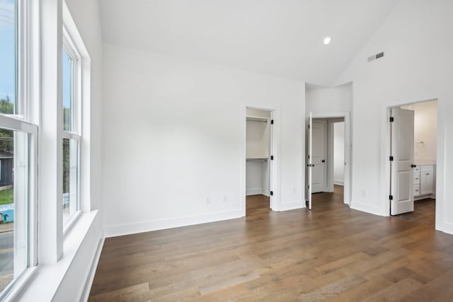 unfurnished bedroom with high vaulted ceiling, dark hardwood / wood-style flooring, a spacious closet, a closet, and connected bathroom