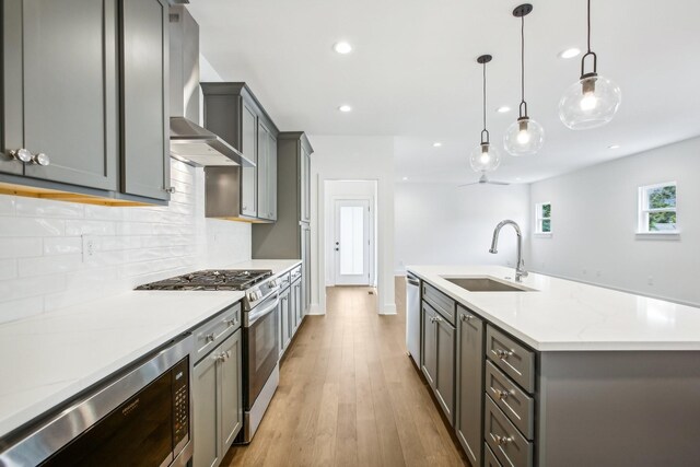 kitchen featuring sink, appliances with stainless steel finishes, light hardwood / wood-style floors, tasteful backsplash, and wall chimney range hood