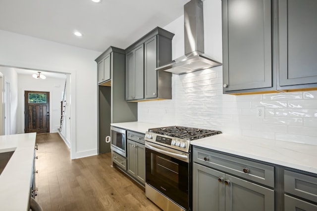 kitchen featuring backsplash, stainless steel appliances, wall chimney range hood, and hardwood / wood-style flooring