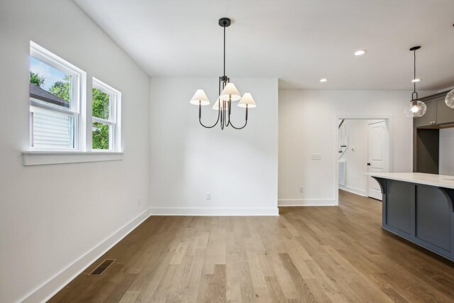 unfurnished dining area featuring light wood-type flooring and an inviting chandelier