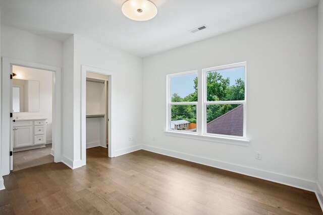 unfurnished bedroom featuring a walk in closet, hardwood / wood-style flooring, a closet, and ensuite bathroom