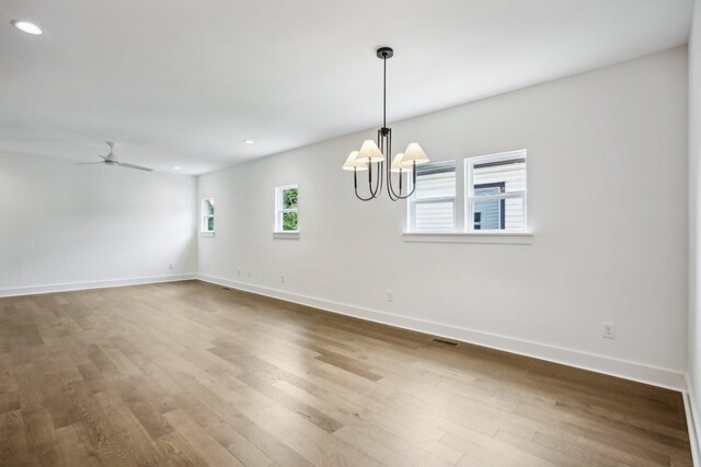 unfurnished room with ceiling fan with notable chandelier and wood-type flooring