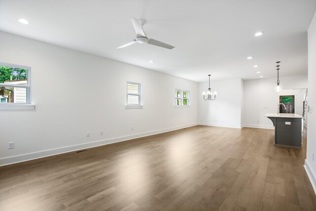 unfurnished living room with ceiling fan with notable chandelier and wood-type flooring