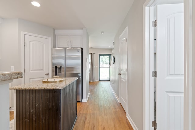 kitchen with stainless steel refrigerator with ice dispenser, white cabinetry, light hardwood / wood-style floors, light stone countertops, and a center island