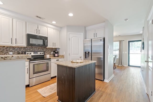 kitchen with light wood-type flooring, stainless steel appliances, a kitchen island, and white cabinets