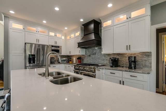 kitchen with backsplash, custom range hood, white cabinets, sink, and stainless steel appliances