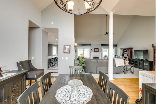 dining space featuring ornate columns, high vaulted ceiling, ceiling fan with notable chandelier, and wood-type flooring